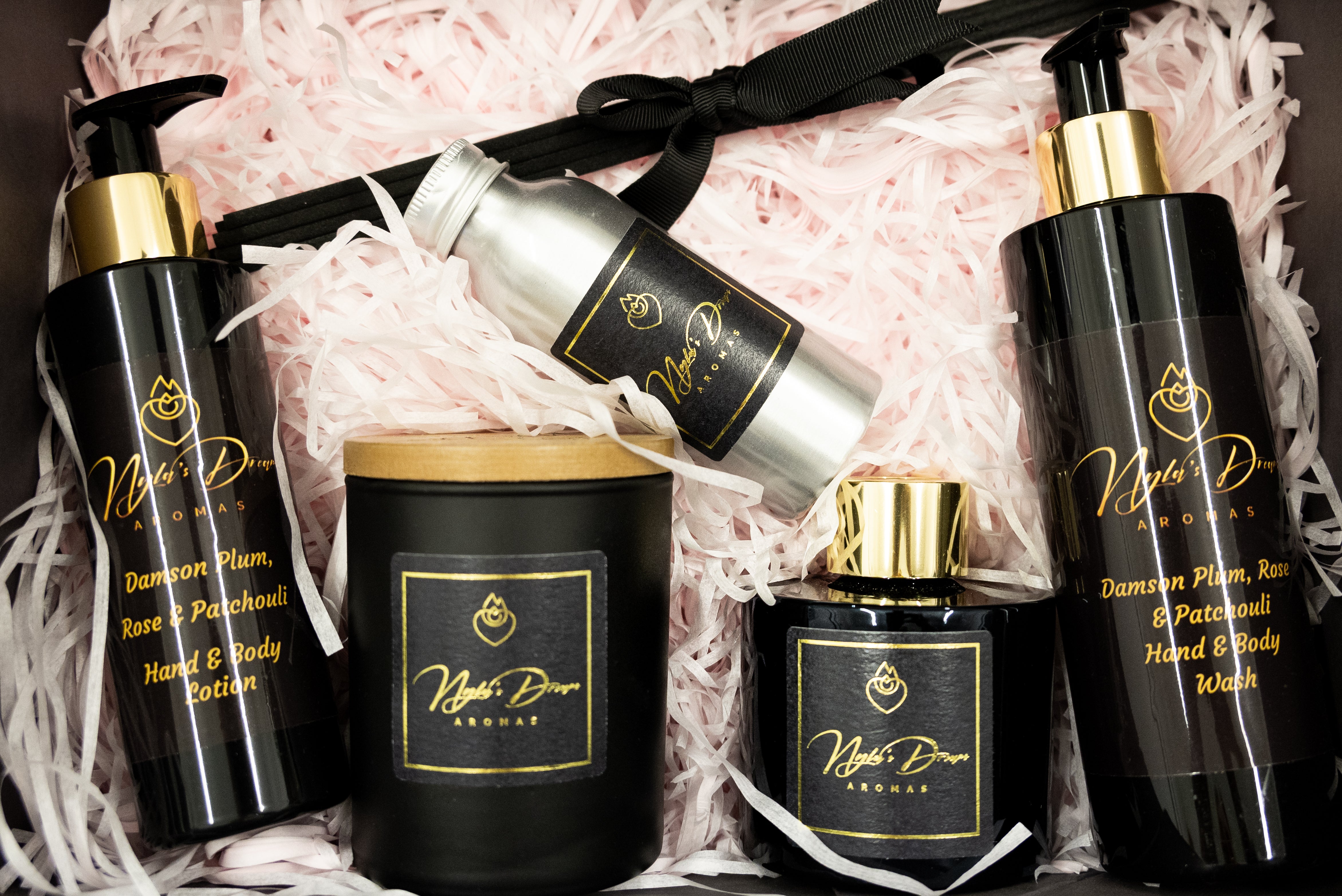 Set of black and gold cosmetic bottles with visible branding on a pink textured background