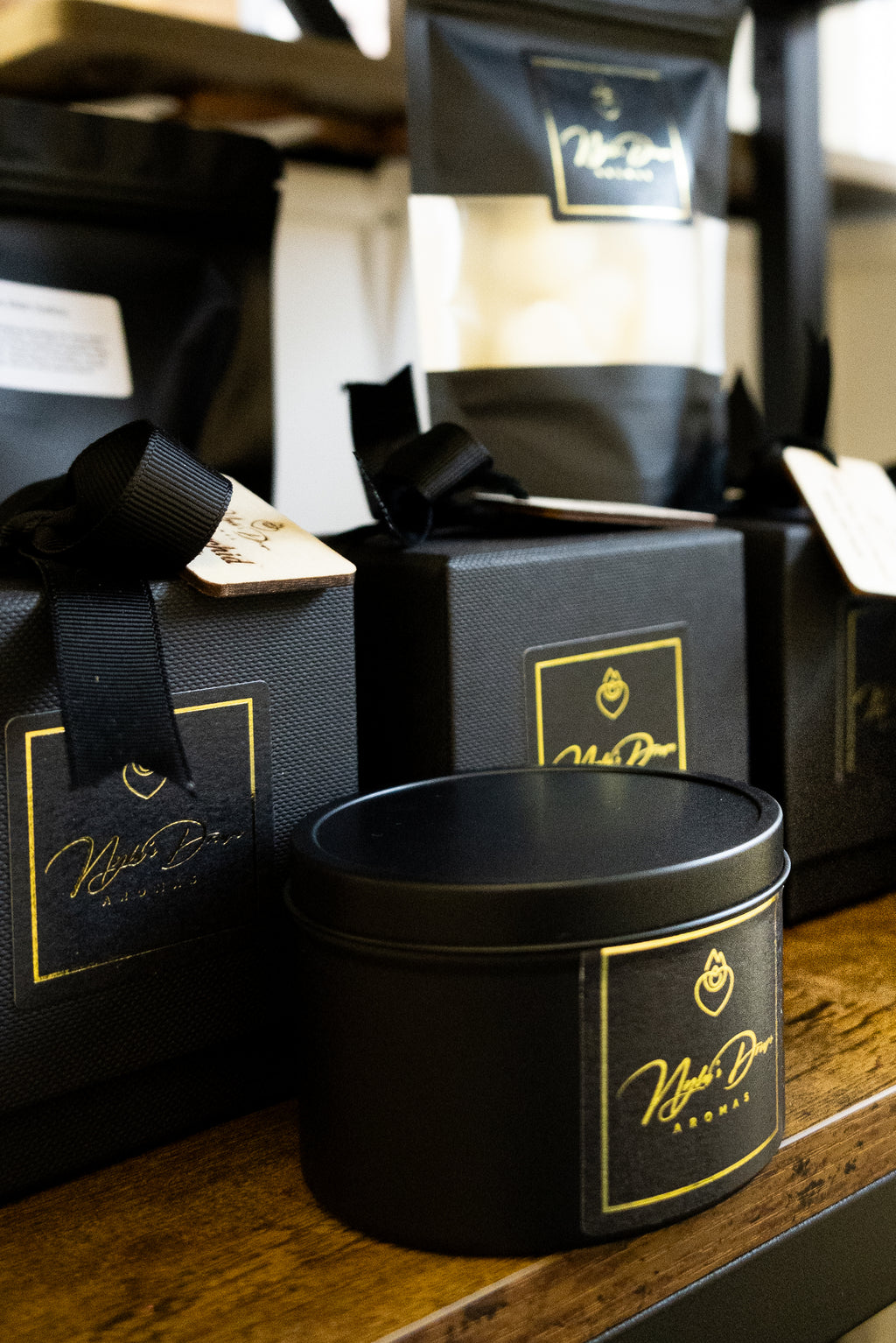 Black gift box with gold label and black tinned candle with gold label on a wooden surface.
