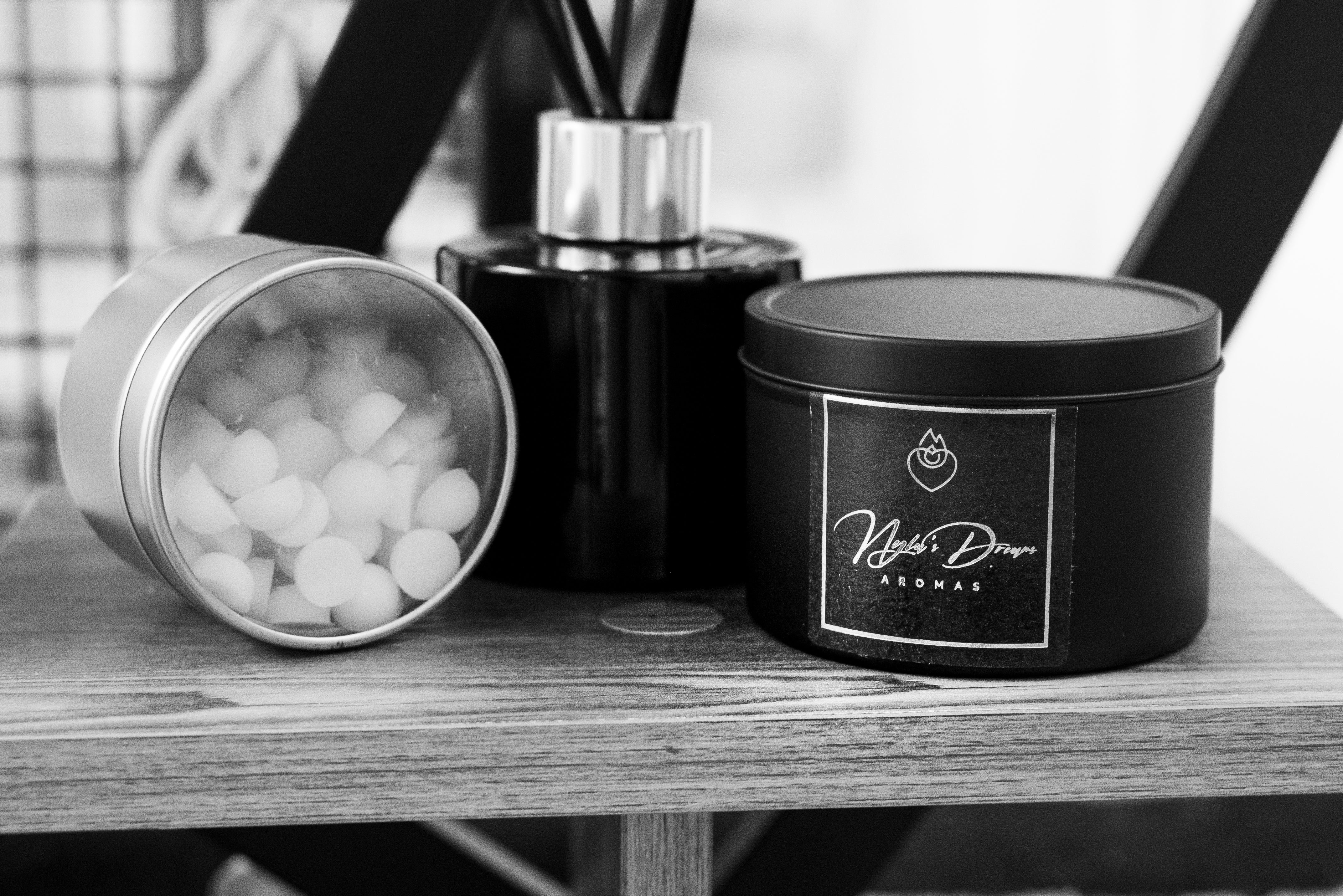 Home fragrance products including a diffuser and containers of wax melt drops on a wooden surface.
